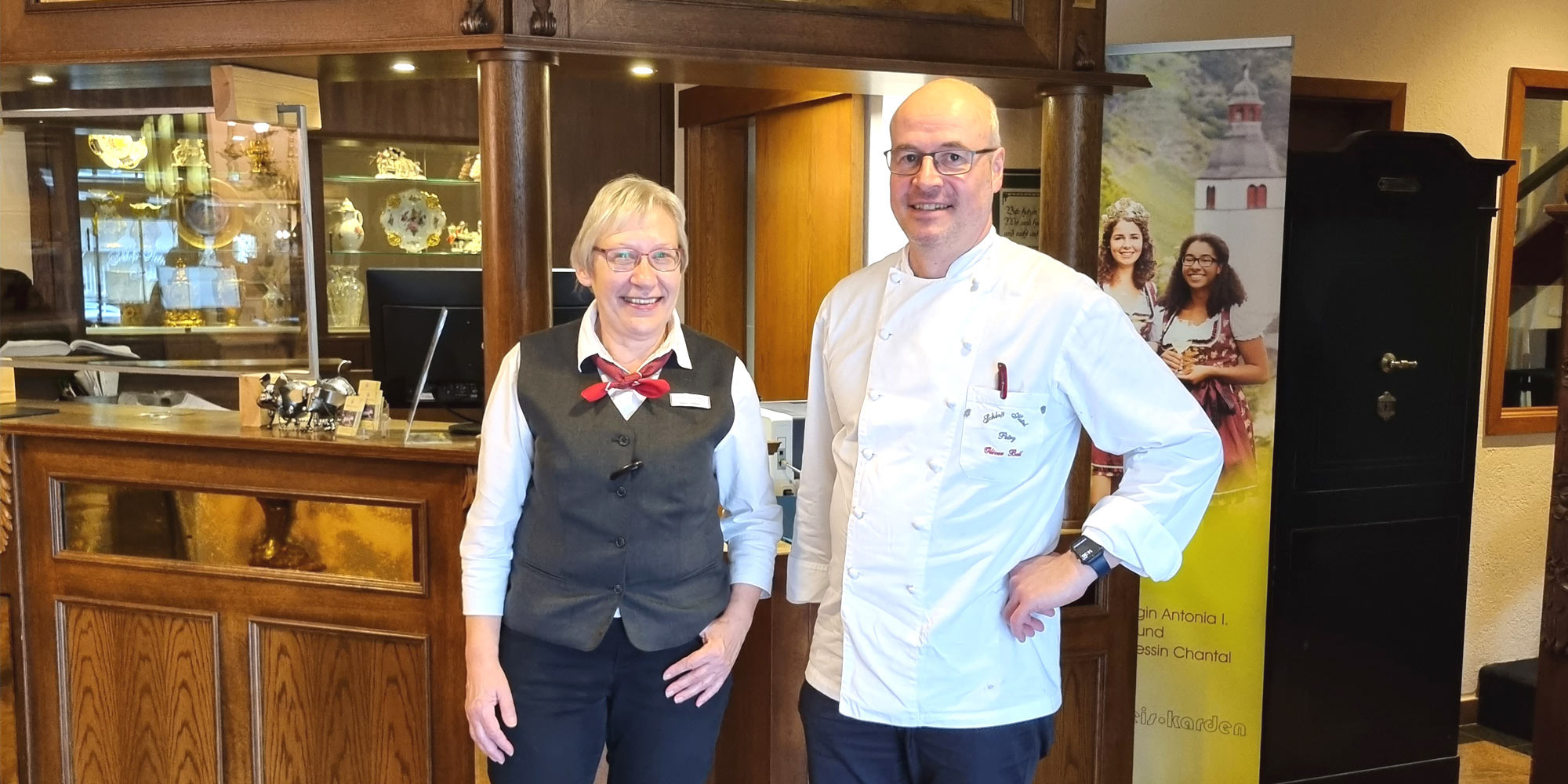 Agnes Höfner und Oliver Bell vom Schloß-Hotel Petry, Partnerbetrieb des Tourismusclusters Eifel Mosel Hunsrück, vor der Rezeption im Hotel